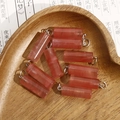 Macro shot of 10 red stone column pendants with metal loops in a heart shaped wood tray - Reddish Brown Strawberry Quartz Style (No. 2)