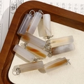 Detailed macro view of natural agate cylinder pendants with silver rings on wood tray - Grey White Textured Agate Style (No. 9)