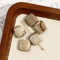 Macro detail van vijf vierkante kralen van natuursteen met gouden naalden op hout - Nr. 16 (Beige-bruin met donkerbruine gevlekte vierkante stijl) (Nr. 16 één stuk)