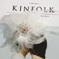Close-up of white feather and mesh headpiece with crystal beads on a magazine - White