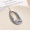 Detailed view of ink-textured drop-shaped acrylic earring with gold hook on a tray - Smoke