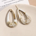 Macro shot of marble-textured acrylic drop earrings with gold studs in a ceramic dish - Milk Tea