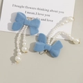 Macro shot of light blue velvet bow earrings with long white faux pearl tassels - Blue