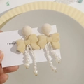 Detail of cream flocked bow earrings with elegant faux pearl tassel on display - Beige