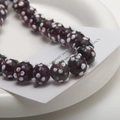 Close-up of handmade dark purple floral glass beads on a white ceramic plate for DIY jewelry - 1 Piece (10x14mm) / Purple