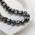 Detailed macro view of handmade floral glass beads with Millefiori art on ceramic tray - 1 Piece (10x14mm) / Black