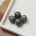Macro detail of 12mm natural stone pendants with silver rings on a white tray - Grey Green