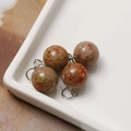 Macro shot of 12mm speckled natural stone bead charms with silver hanging loops - Dark Color