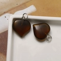 Detail of two translucent amber heart pendants with polished finish and silver jump rings - Tiger Eye Heart
