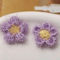 Nahaufnahme von häkelblumen in lila und gelb mit glitzerndem silberfaden und flauschiger optik - Lila