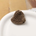 Close-up of brown hand-knitted mini hat accessory on a white plate with woven texture - Brown