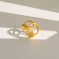 Détail d'une bague dorée ajustable au design circulaire entrelacé sur fond en cuir crème - Style Imbriqué Arrondi Géométrique (186)