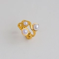 Primo piano di anello a onde in oro opaco con tre perle bianche su sfondo in pelle - Stile Tripla Perla Ondulato (347)