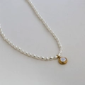 Collana di perle placcata oro con ciondolo bianco tondo su sfondo grigio minimal - Stile Ciondolo con Perla Rotonda (C-1-54)