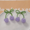 Macro view of handmade purple beaded cherry earrings with green crystal bow details - Purple