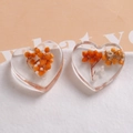 Macro view of transparent resin heart charms with orange dried flowers and white pearls - Yellow Dried Flowers