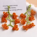Handmade woven glass bead flower pendant with orange petals and green stems on white plate - Orange