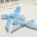 Close-up of light blue velvet bow hair clips on a clean white background with a newspaper - Light Blue