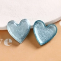 Macro shot of two light blue resin heart charms with silver glitter on white textured stone - Light Blue Heart