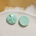Macro view of mint green resin windmill charms on a textured white ceramic background - Green