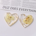 Primer plano de dijes de resina en forma de corazón con flores secas y pan de oro - Estilo Pétalo