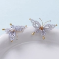 Macro shot of handmade blue beaded butterfly earrings with gold wire and pearl accents - Light Blue