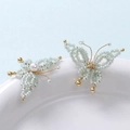Macro view of handmade light blue beaded butterfly earrings with white pearl detail - Light Green