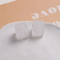 Détail macro de clous d'oreilles carrés en résine pailletée de 16mm sur assiette blanche - Blanc