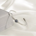 Dettaglio ravvicinato di un bracciale rigido Evil Eye argento su seta bianca - Argento