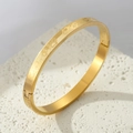 Gold-plated titanium steel bangle with engraved heart patterns on stone background - Gold