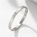 Detail of silver stainless steel bangle showing geometric Greek key patterns and side hinge - Steel