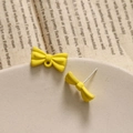 Close-up of matte lemon yellow bow earrings with silver pins on a ceramic dish - Yellow