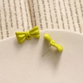 Detailed macro shot of bright yellow matte bow earrings on a vintage textured tray - Green