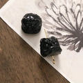 Dettaglio macro di due ciondoli neri intagliati a forma di leone su superficie di legno - 1 Pezzo / Nero