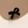 Close-up of black flocked velvet bow earrings on textured leather and beige background - Black