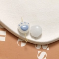 Macro detail of hand-painted cat paw glass charms with gold metal clips on textured tray - Blue