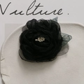 Detailed macro of a black mesh camellia flower brooch with pearl center and green leaves - Black