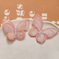 Détail de patchs papillons brodés en dentelle rose orangé sur une assiette en céramique - Orange