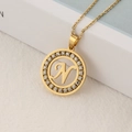 Gold round pendant necklace with letter N and sparkling crystals on white book edge - Letter N
