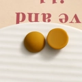 Macro shot of 15.5mm ginger yellow matte resin semi-spheres on a white ceramic plate - Round Mustard