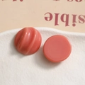 Macro shot of coral pink resin jewelry charms with spiral texture on a ceramic tray - Orange Red