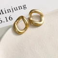 Macro view of matte gold irregular C-shape earrings on a minimalist white ceramic tray - Irregular Style