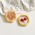 Dettaglio di orecchini in resina crema con fiori secchi rosa e foglia d'oro in posa - Giallo
