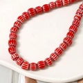 Macro di perline in ceramica rosse con strisce bianche su un piatto di ceramica bianca - Rosso