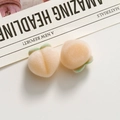 Close-up of peach-shaped flocked resin charms with green leaves for DIY jewelry making - Orange
