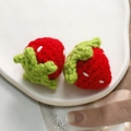 Macro detail of hand-knitted strawberry charms in red and green yarn on white ceramic - Big Strawberry