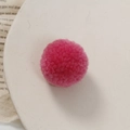 Detail van een pluizige roze pompon op een beige bord voor doe-het-zelf handwerkprojecten - Rozerood