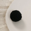 Macro-opname van een 3cm zwarte pluche pompon op een vintage boek voor DIY-projecten - Zwart