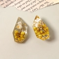 Detailed macro view of resin charms with yellow dried flowers and gold foil elements - Yellow