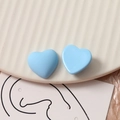 Macro-opname van mat hemelblauwe hartvormige oorknopjes op een wit keramisch bord - Blauw